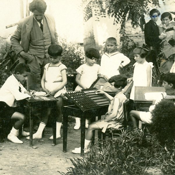 Α' τάξη Προτύπου, Ιούνιος 1928. Ομάδα παιδιών του Προτύπου εργάζεται στο ύπαιθρο. Ο Μίλτος Κουντουράς, η Αλεξάνδρα Κεσσανλή και τελειόφοιτες του Διδασκαλείου παρακολουθούν την εργασία των παιδιών.