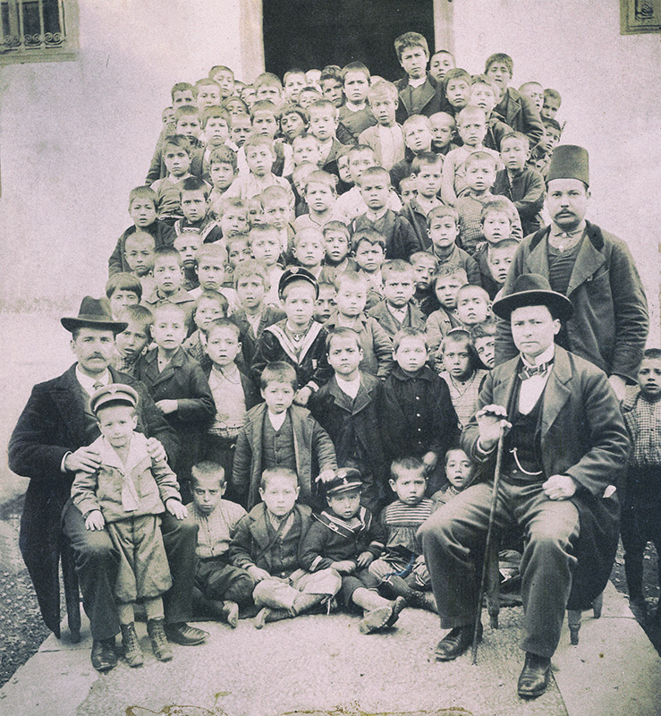 Φεβρουάριος 1903. Δημοτικό Σχολείο Σκοπέλου Γέρας. Ο μαθητής Παναγιώτης Γ. Κουντουράς, μικρότερος αδελφός του Μίλτου Κουντουρά, όρθιος, πίσω ακριβώς από το καθιστό, στην πρώτη σειρά, παιδάκι με το "ναυτικό" καπέλο. Φωτογράφος : Ι. Γ. Φεργαδιώτης, Φωτογράφος Σμύρνης.